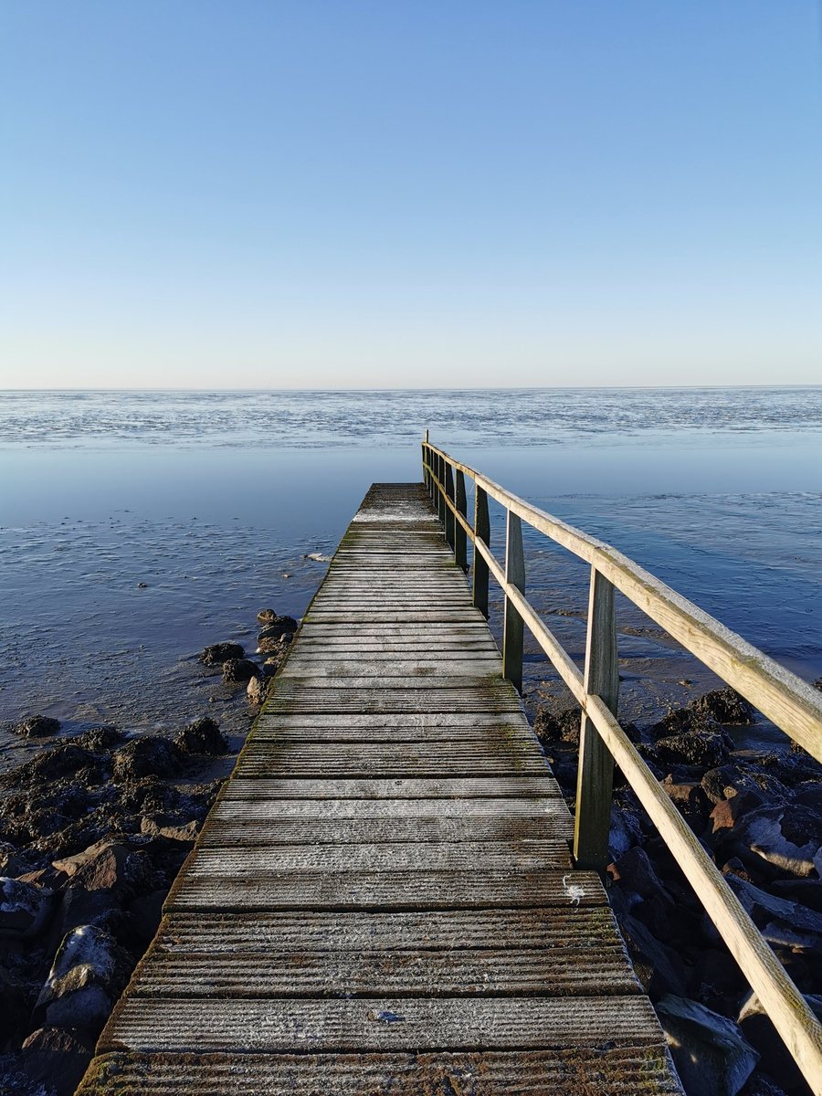 Holzsteg führt über das ruhige Wasser zum Horizont